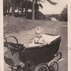 Photo:Baby Linda in her pram with the huts behind